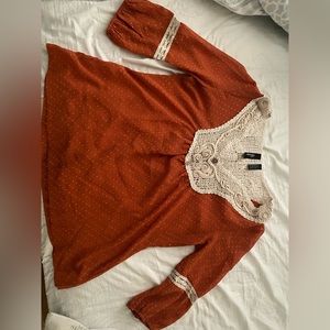 It’s a shade of orange blouse. Very pretty designs. Sheer fabric with no give.